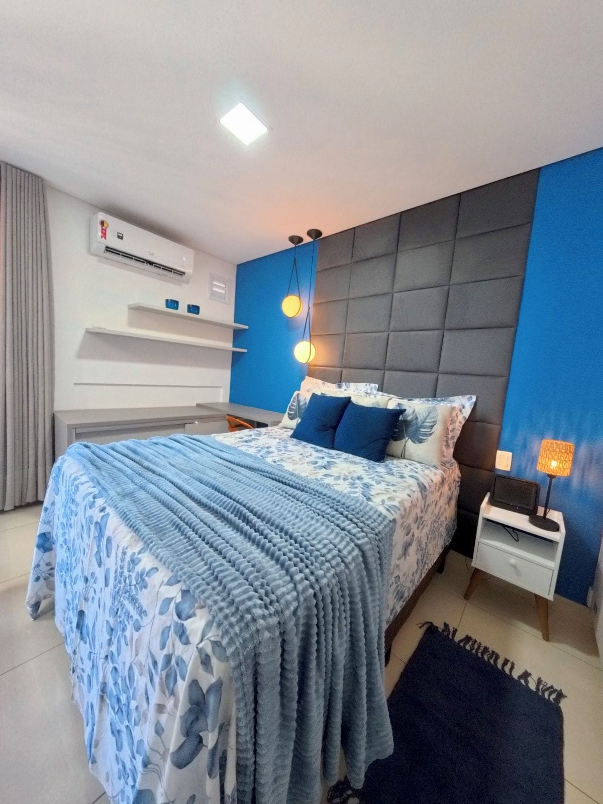 A modern bedroom with a bed, bedside tables, an air conditioning unit, and a nightstand with a lamp.