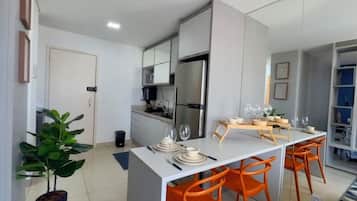 Une cuisine moderne avec un îlot central, des chaises orange et une table à manger pour quatre personnes.