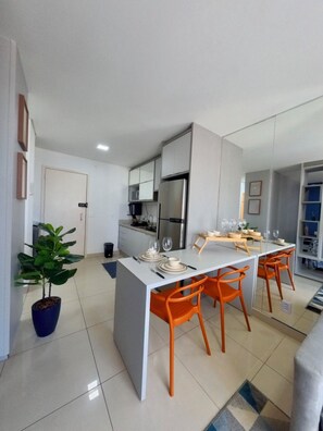 Une cuisine moderne avec un îlot central, des chaises orange et une table à manger pour quatre personnes.