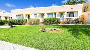 A building with a flat roof, multiple windows, and a well-maintained lawn with a grill and circular flower beds. - Cozy Beach Studio Pool and Free Parking (Hollywood)