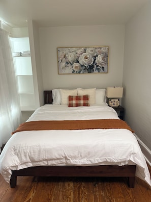 Un dormitorio con una cama, una mesita de noche, una lámpara y un cuadro con motivos florales en la pared.
