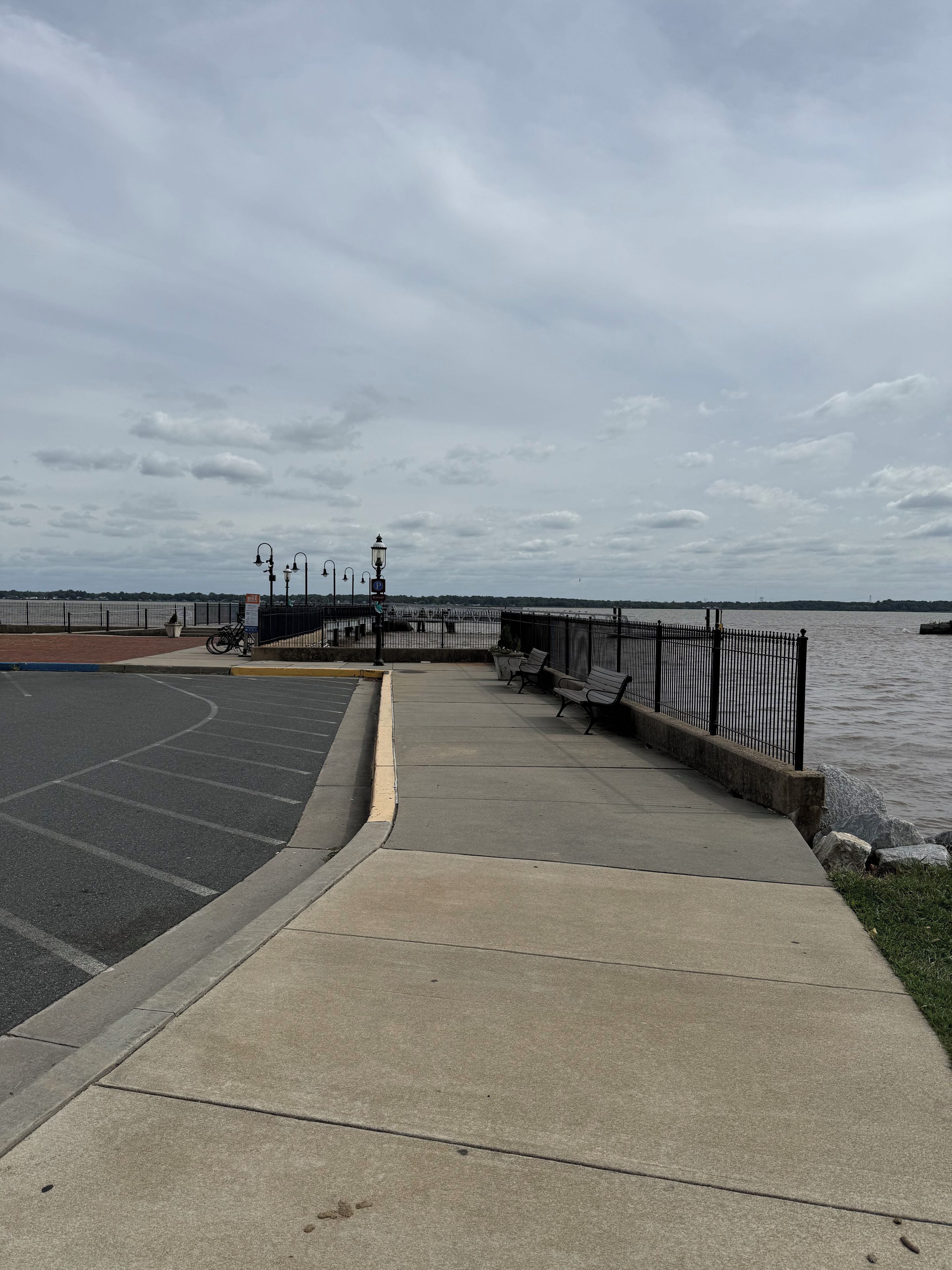 A waterfront promenade with a paved walkway, benches, and a bike rack.