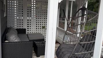 Ett takförsett utomhusområde med sittplatser, en soffa i rotting, en hängstol och en mönstrad matta.
