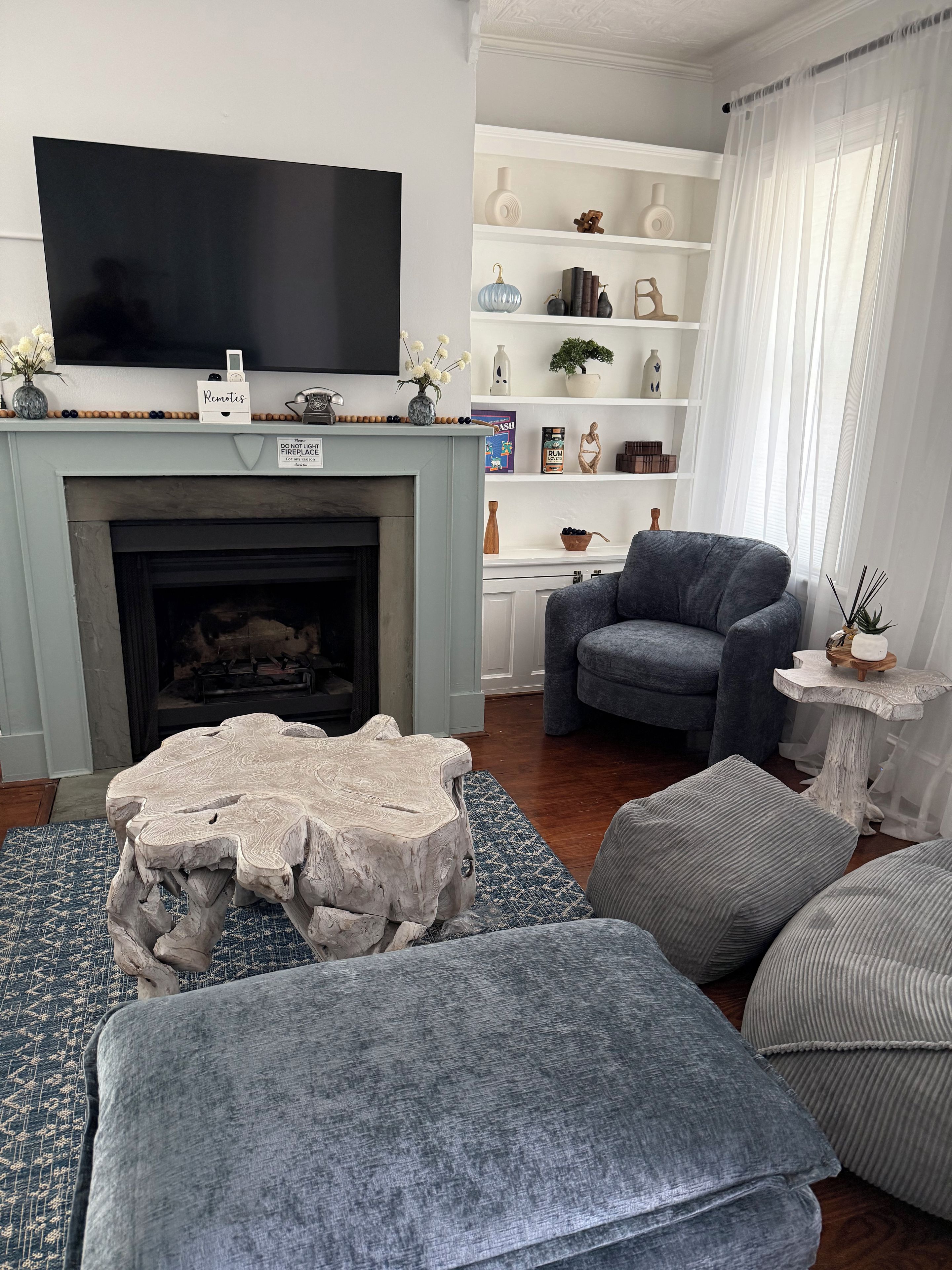 Ein Wohnzimmer mit Kamin, Fernseher und einer Sitzecke mit Poufs und einem Sessel.