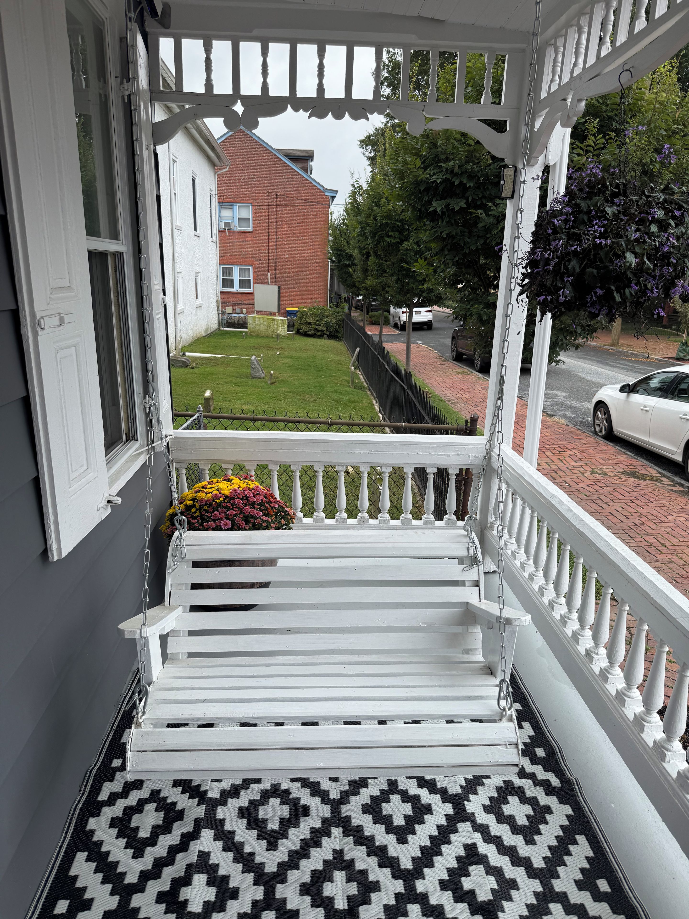 A white porch with a patterned rug, a white bench, and a flower pot.