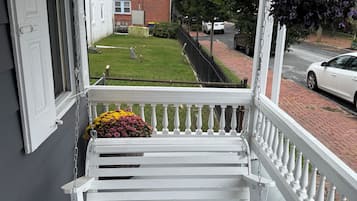 A white porch with a patterned rug, a white bench, and a flower pot.