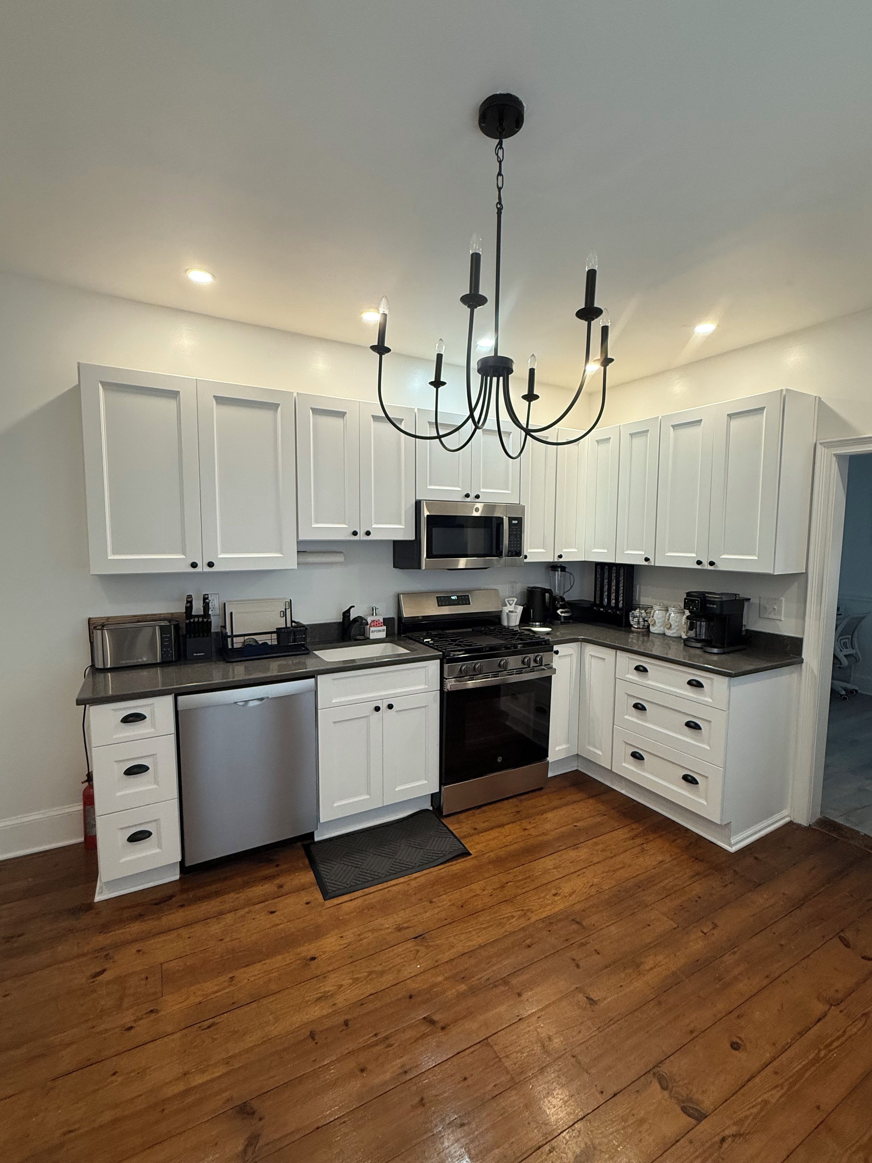 A modern kitchen with white cabinetry, a stainless steel range, a microwave, and a black chandelier.