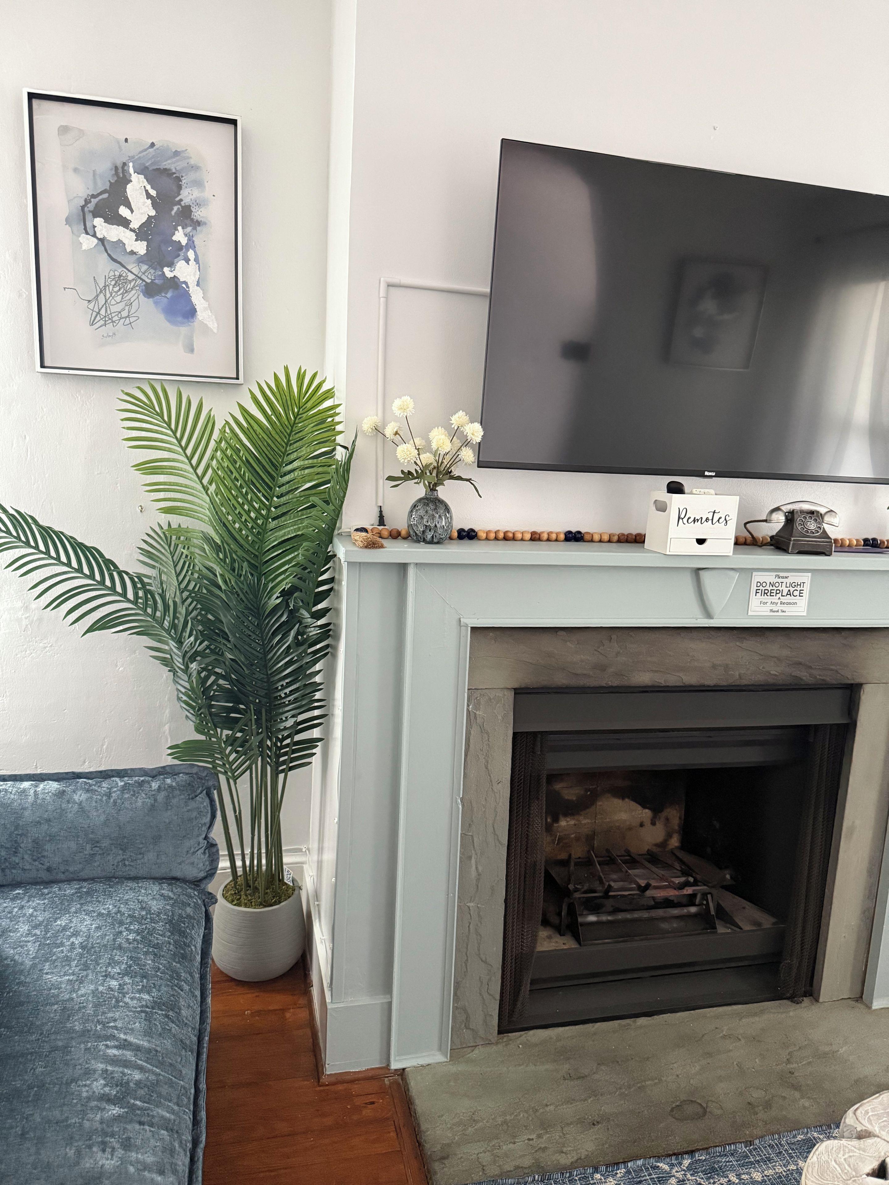 Una sala de estar con chimenea, televisor montado en la pared, un cuadro abstracto enmarcado y una planta en maceta.