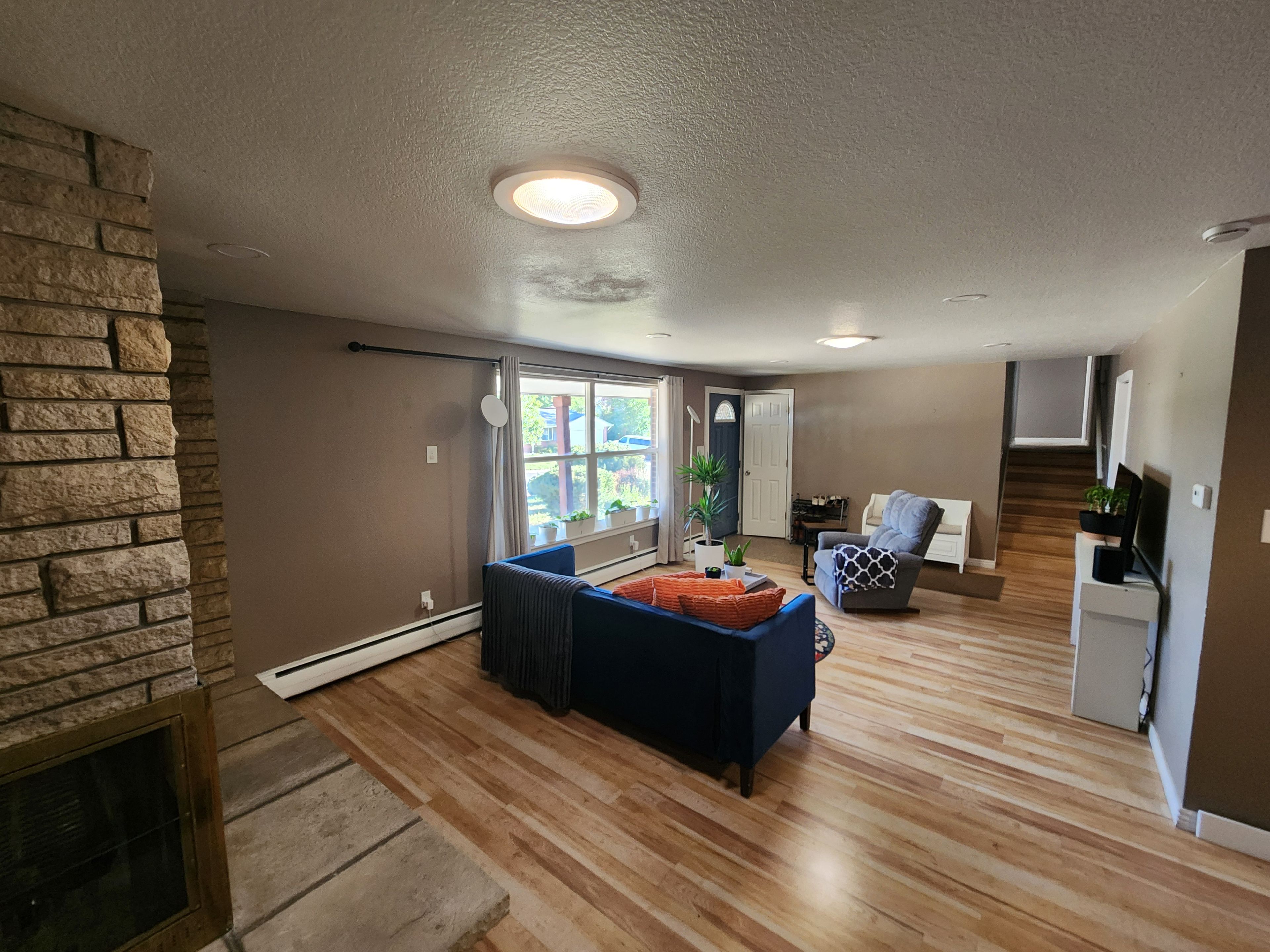 Un salon avec un mur en pierre, une cheminée, un canapé bleu et un plancher en bois.