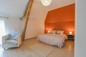 Une chambre avec un plafond en pente, un lit recouvert d’une couverture à rayures, une table de chevet avec une lampe et une chaise avec une couverture.