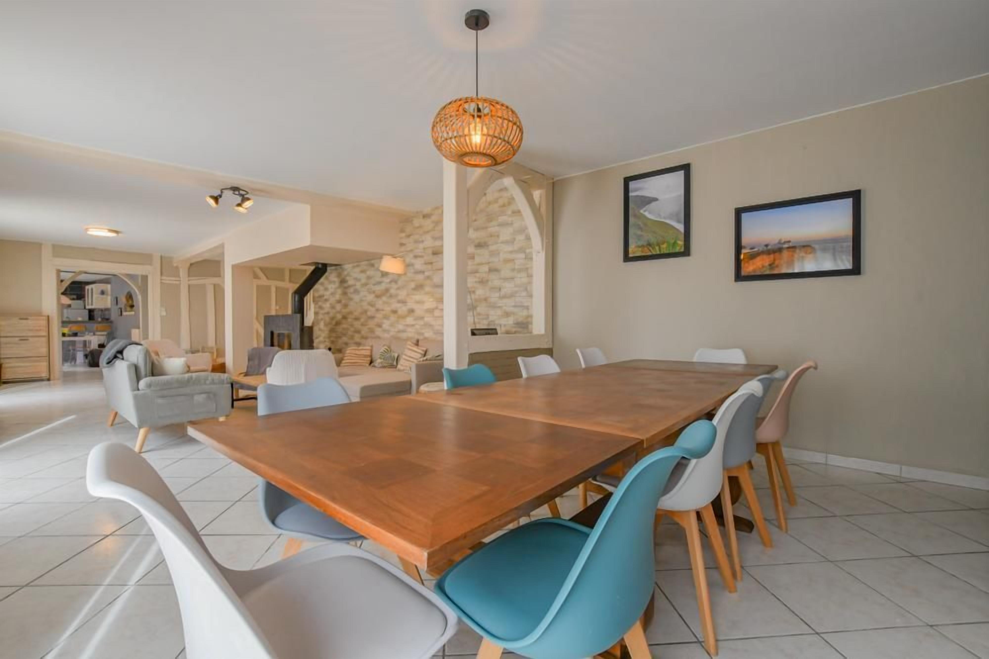 A spacious dining area with a wooden table and modern chairs, a hanging light fixture, and a stone wall with a fireplace.