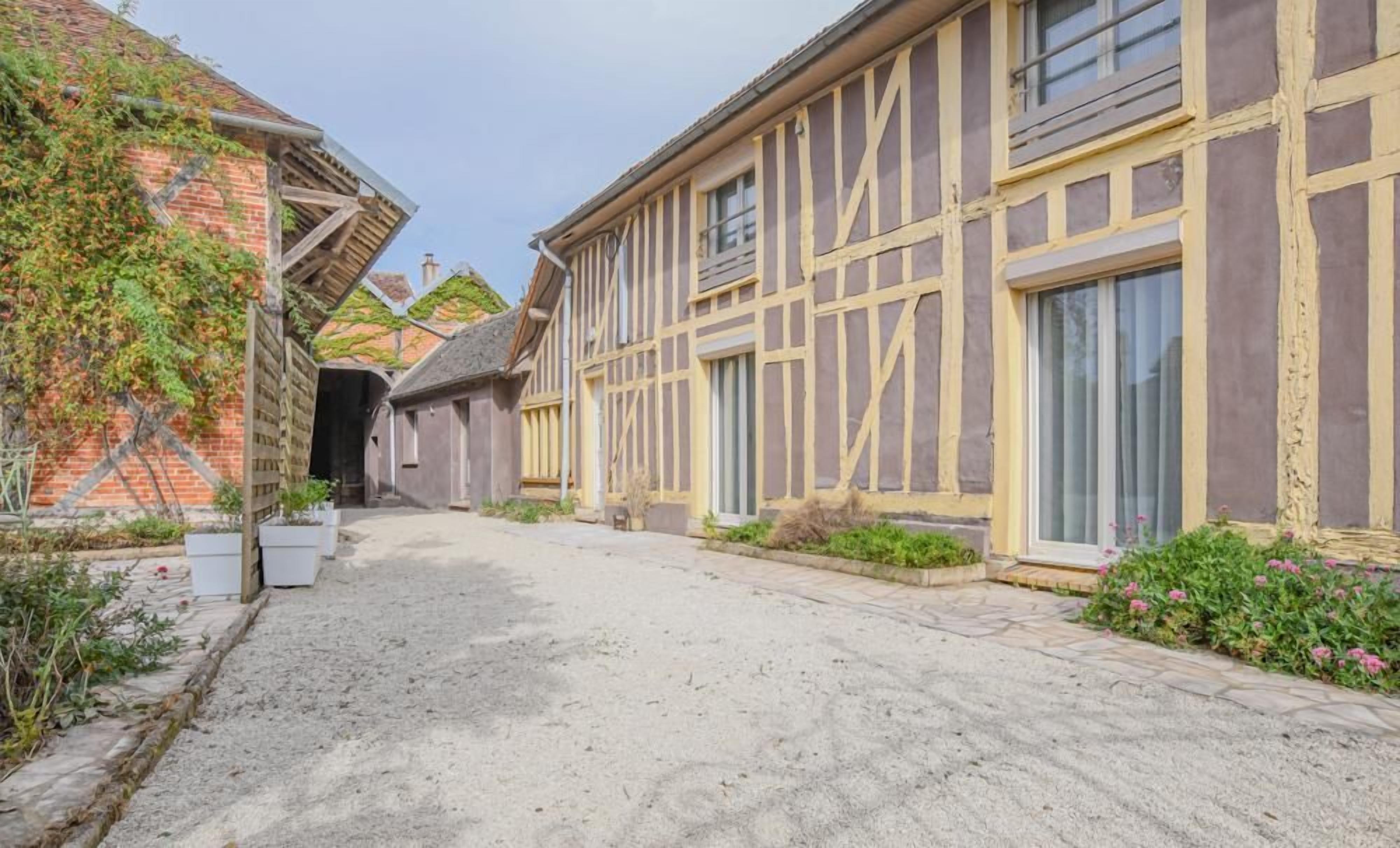 Une rue étroite bordée de bâtiments traditionnels à colombages, un chemin de gravier et des plantes en pot.