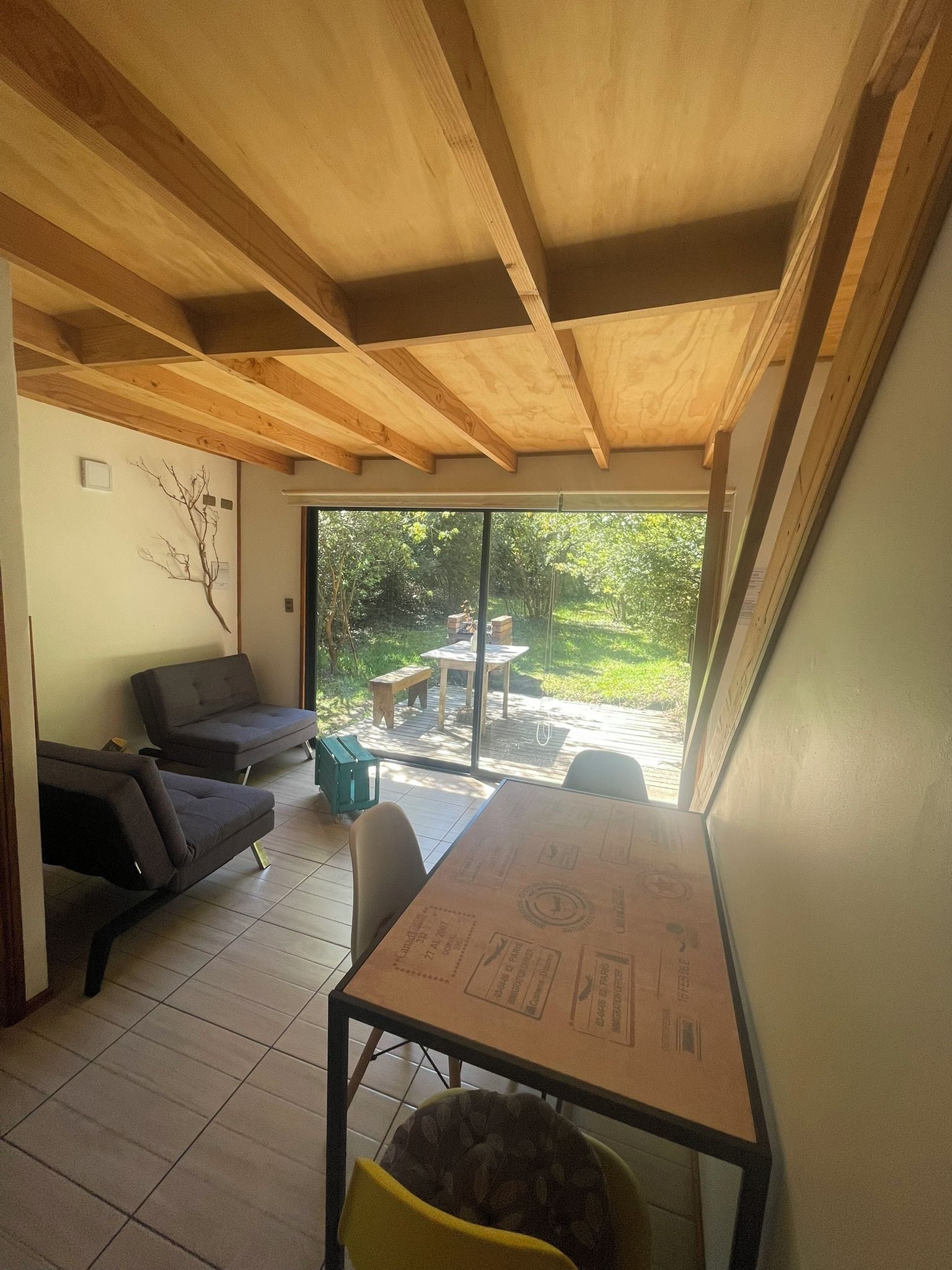 Una habitación con techo de madera, una mesa de comedor, un sofá y vistas a un jardín a través de un ventanal.