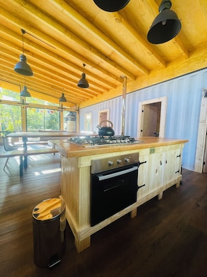 A spacious kitchen with wooden cabinets, a gas stove, and pendant lighting. - Pucura Eco Lodge (Panguipulli)