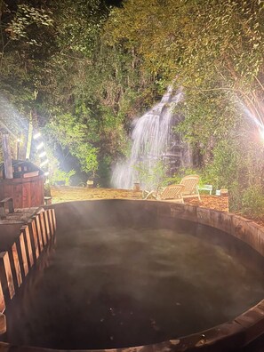 Un manantial de aguas termales rodeado de exuberante vegetación y una cascada.