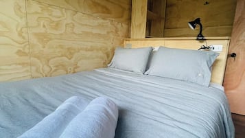 Una cama con ropa de cama gris y dos toallas blancas enrolladas.