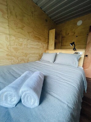 Una cama con ropa de cama gris y dos toallas blancas enrolladas.