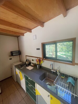 A compact kitchen with a built-in stove, a sink, and a window overlooking greenery.