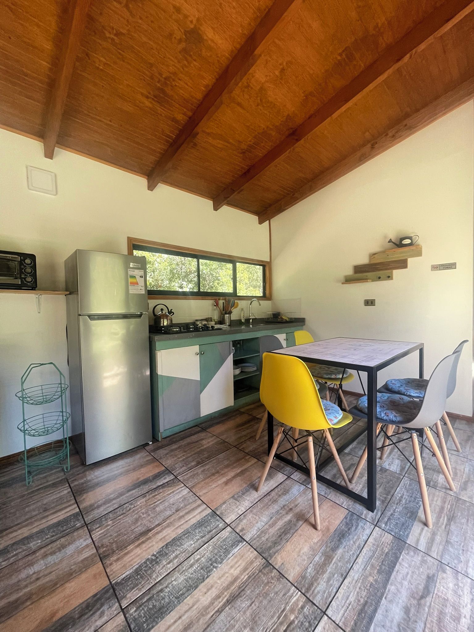 Cocina compacta con refrigerador, estufa y microondas. Hay una mesa de comedor con sillas y un ventanal sobre el lavamanos.