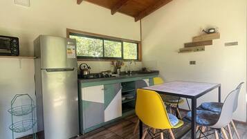 Cocina compacta con refrigerador, estufa y microondas. Hay una mesa de comedor con sillas y un ventanal sobre el lavamanos.