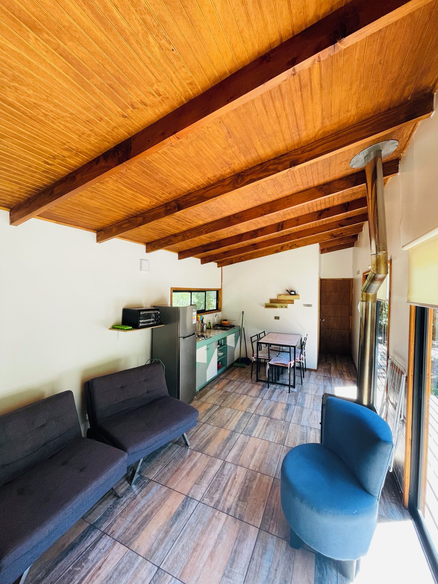 Uma sala de estar ampla com teto de madeira, uma mesa de jantar com cadeiras e uma cozinha equipada.