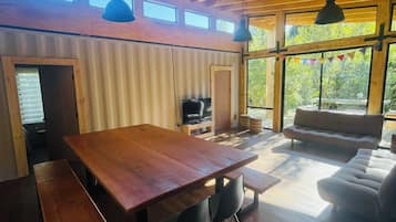 Una habitación amplia con techo de madera, una gran mesa de comedor con bancos, un sofá y un televisor.