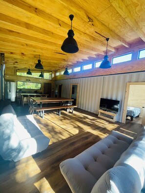 Un salón comedor amplio con techo alto, vigas de madera, un sofá grande, una mesa de comedor y un televisor.