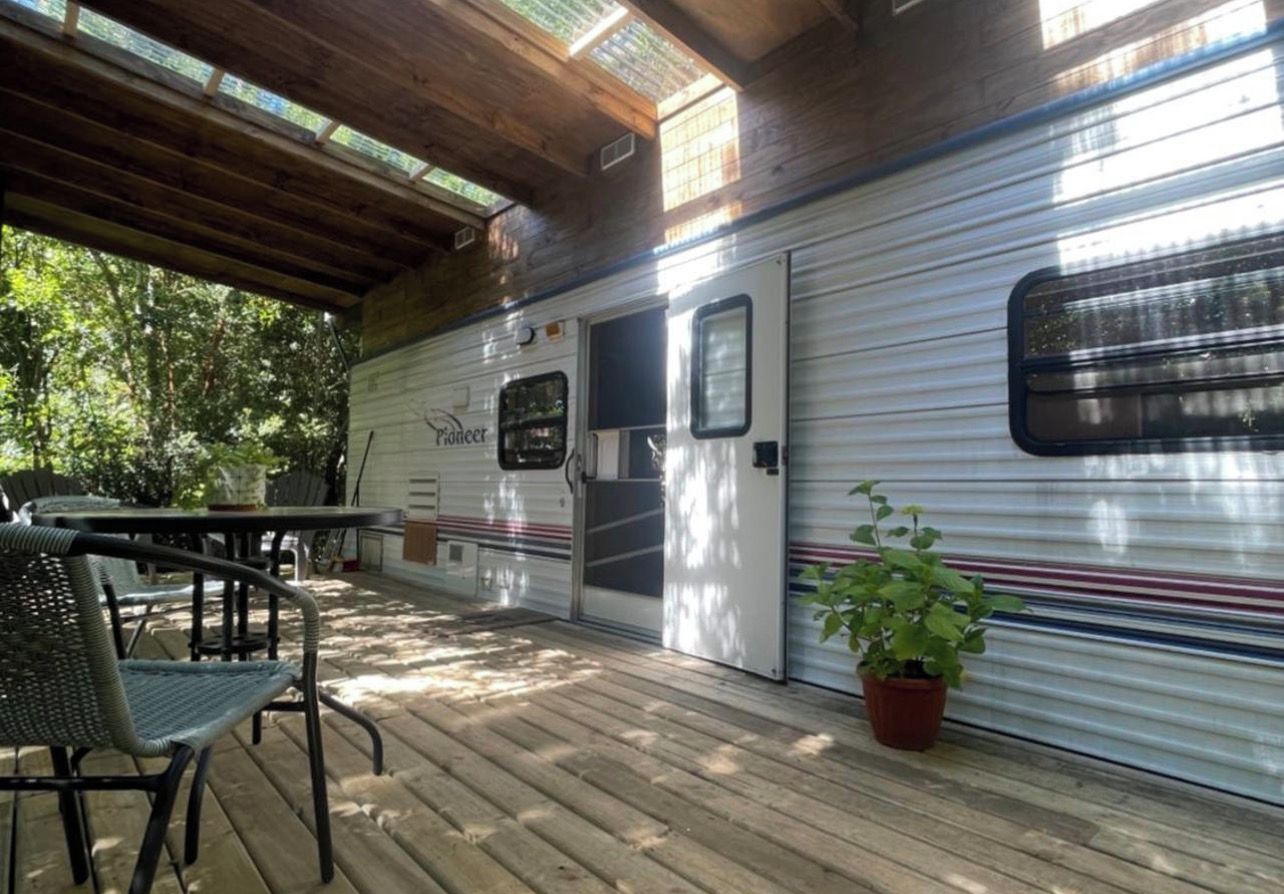 A covered outdoor area with a dining table and chairs, a potted plant, and a Pioneer RV.