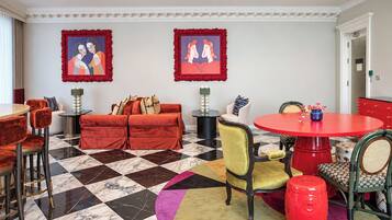 A hotel room with a checkered floor, a red sofa, a round red table, and two framed artworks on the wall.