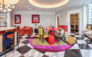 Un vestíbulo de hotel con suelo a cuadros, una zona de bar, arreglos de asientos y obras de arte en las paredes.