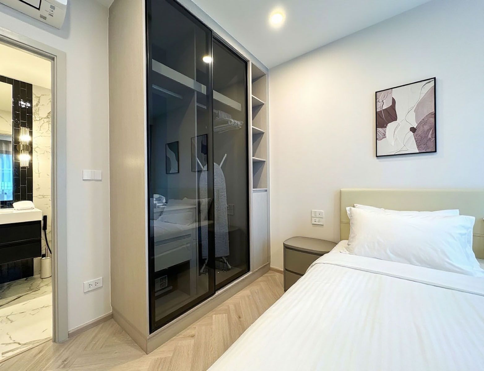 Un dormitorio moderno con cama, vestidor y baño con espejo y lavamanos.