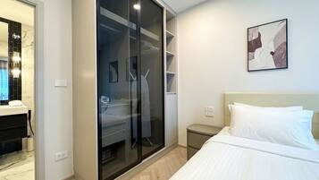 Un dormitorio moderno con cama, vestidor y baño con espejo y lavamanos.