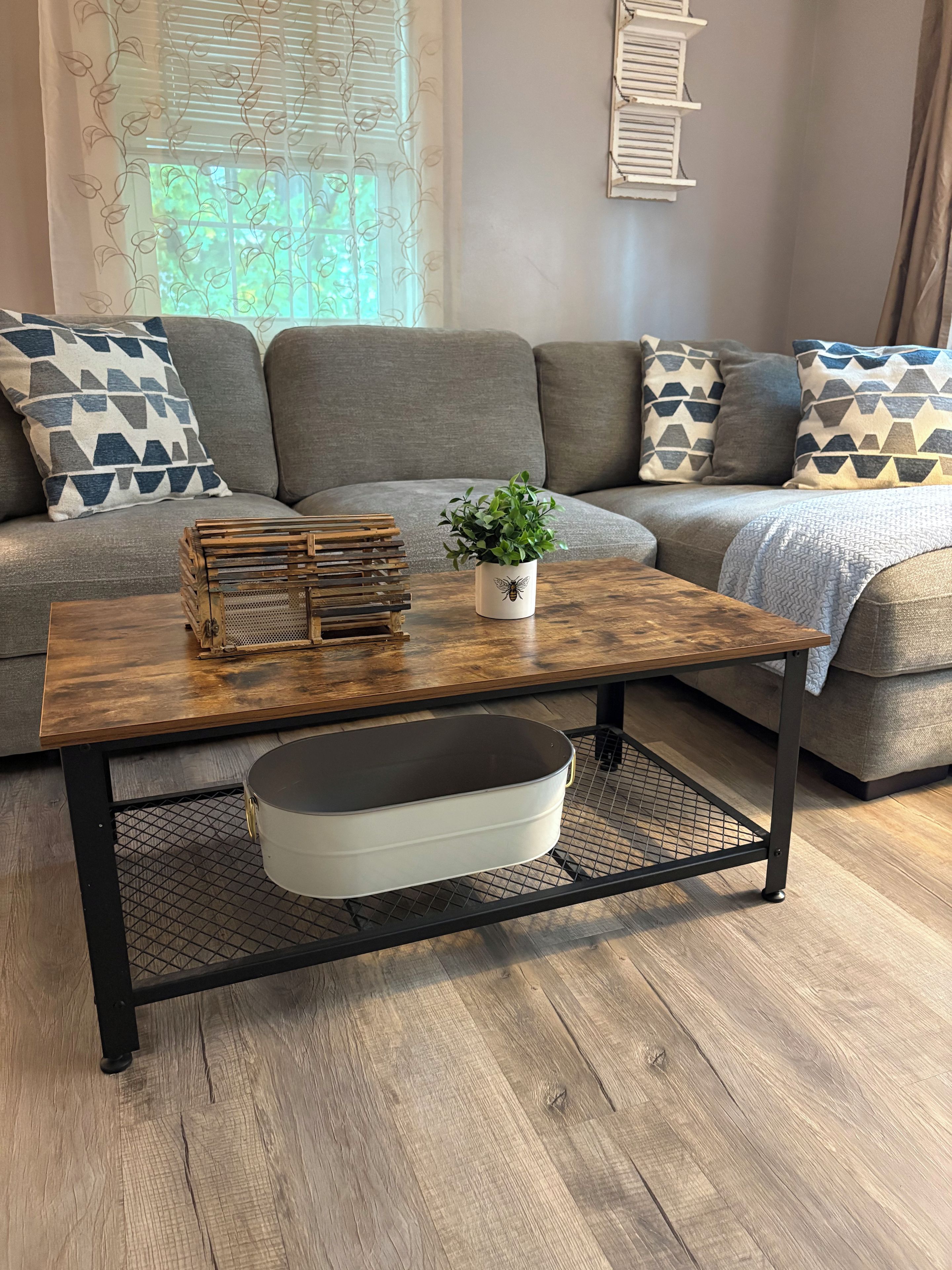 Un salón con sofá, cojines estampados, una mesa de centro con una planta y un objeto decorativo.