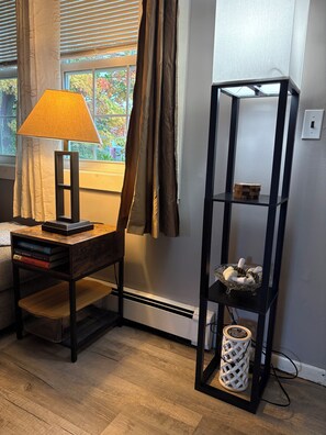 Une pièce avec un plancher en bois, un bureau avec une lampe, une bibliothèque et une fenêtre avec des rideaux.
