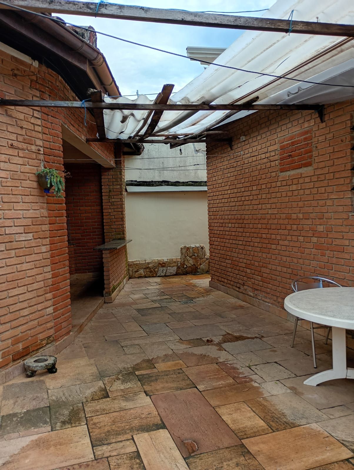 A brick patio with a stone floor, a white table, and a covered area with a metal roof.