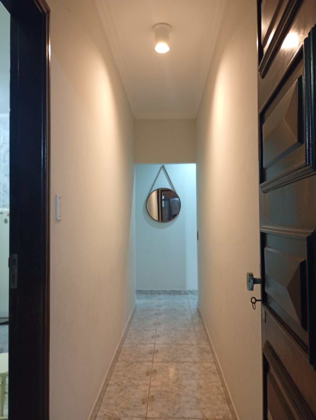 A hallway with a light fixture on the ceiling, a door with a handle on the right, and a wall-mounted mirror.