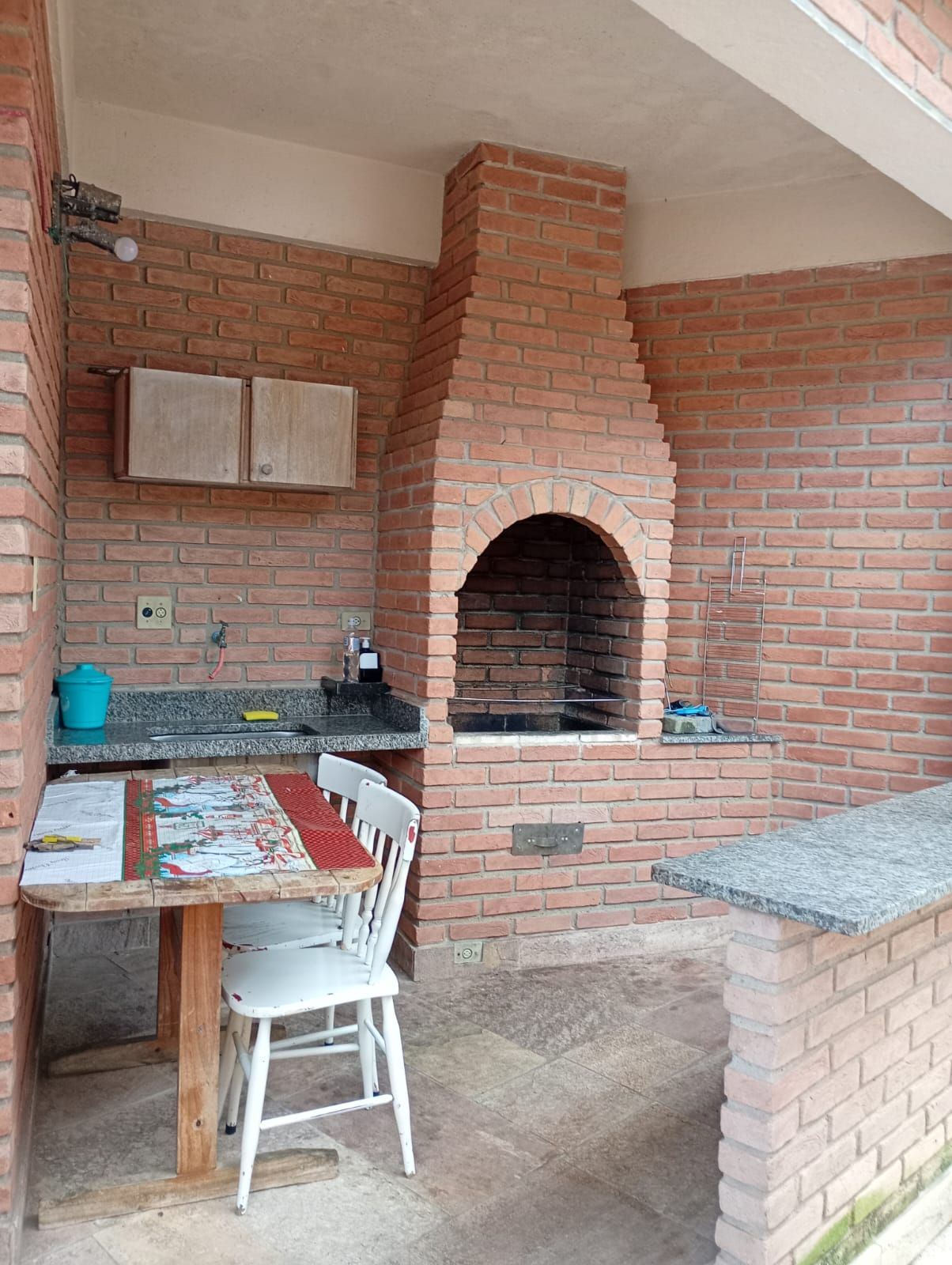 Et udendørs køkken i mursten med grill, et bord med en stol og en bordplade.