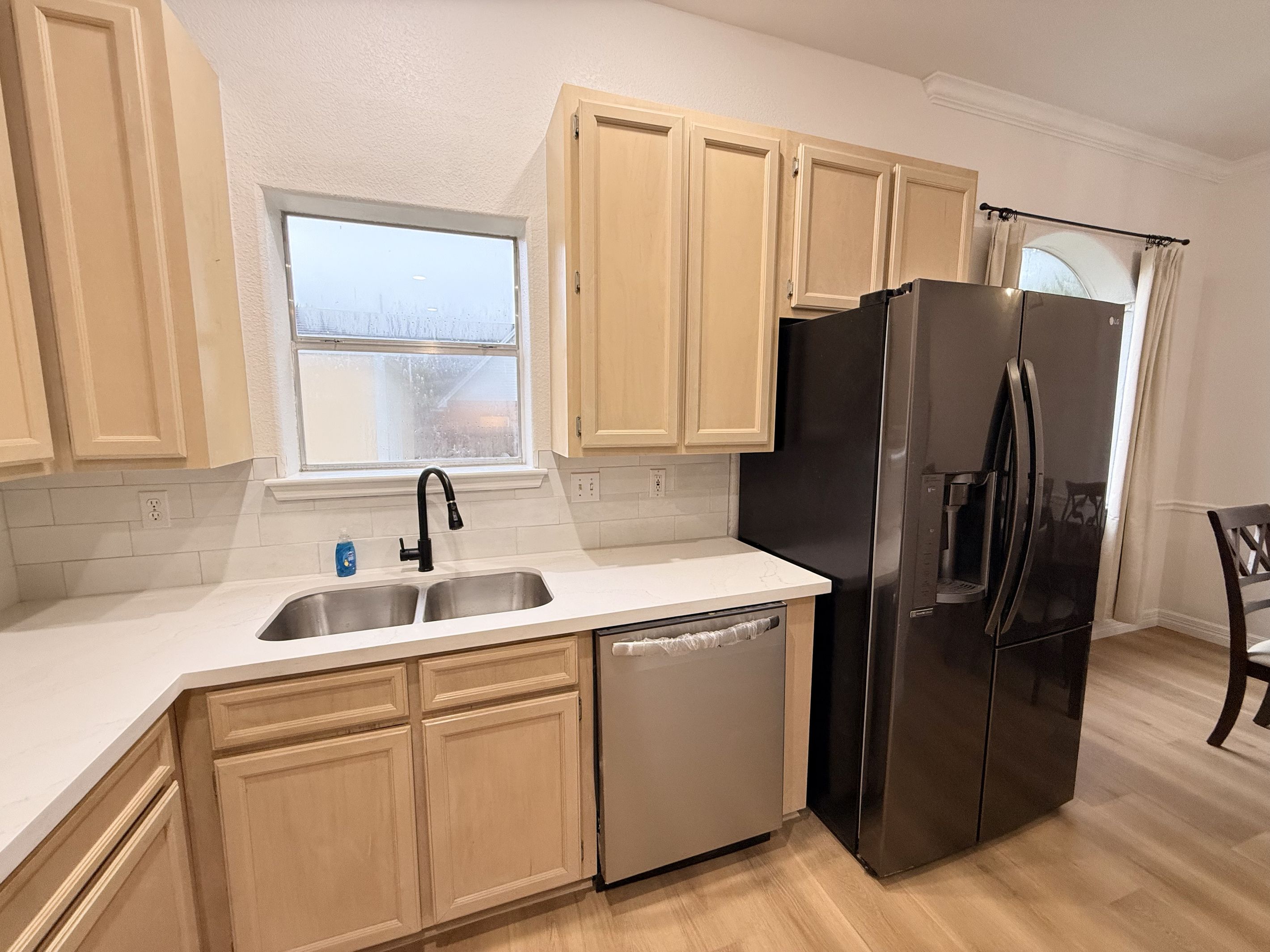 Una cocina con armarios de madera clara, un refrigerador de acero inoxidable, un lavavajillas y una ventana que proporciona luz natural.