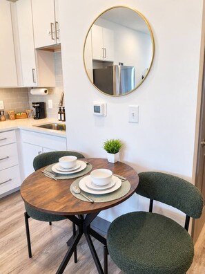 A compact kitchen with white cabinets, a round mirror, a small potted plant, and a dining table with two chairs. - *New* Suite Perfect DT Location I Gym and Rooftop (Atlanta)