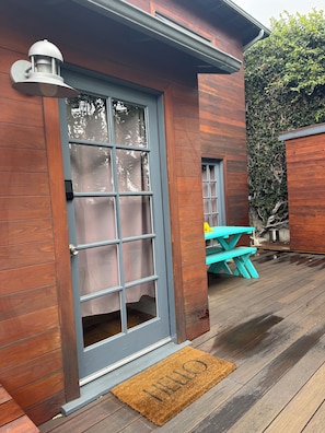 A wooden exterior with a sliding glass door, a blue outdoor bench, and a doormat. - Cozy Tuck-Under Studio in Silver Lake w/ Private Tropical Yard, Orange Trees (Los Angeles)