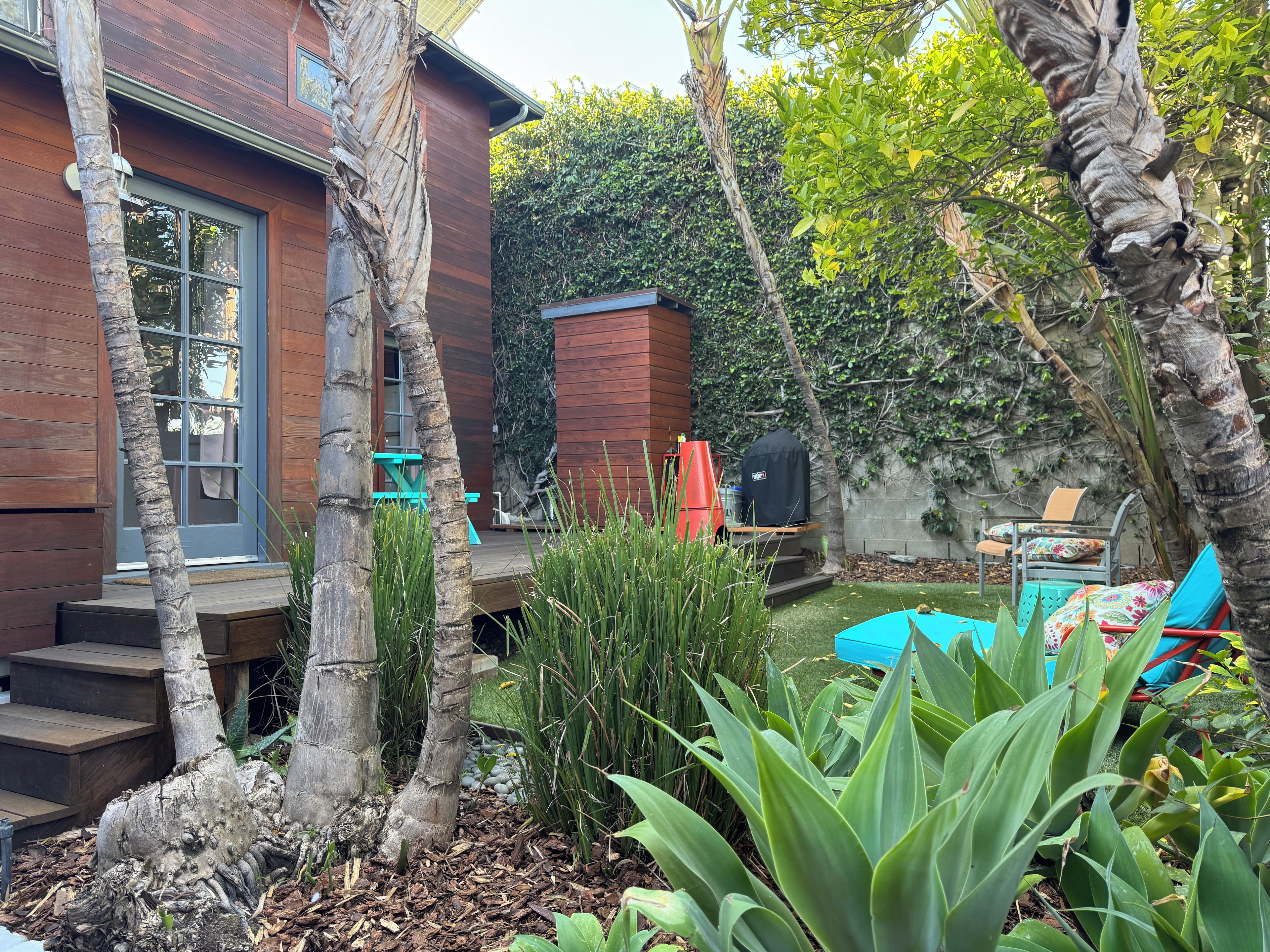 A wooden house with a patio, outdoor furniture, and a garden with various plants.