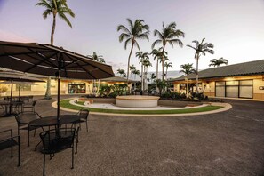 An outdoor courtyard with palm trees, a circular seating area, and outdoor dining tables. - Luxury Villa Designer updates HI Gem Kings (Waimea)