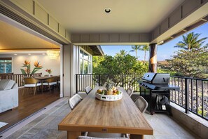 Een houten eettafel met een fruitmand, een grill en terrasmeubels met stoelen.