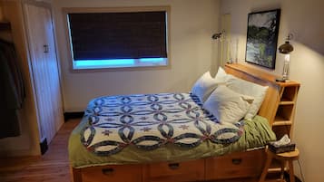 A bedroom with a bed, a window, a nightstand, a lamp, and a painting on the wall.