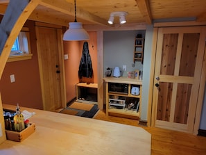 Een gezellige kamer met een houten plafond, een hanglamp, een bankje, een deur en een plank met keukenapparatuur.