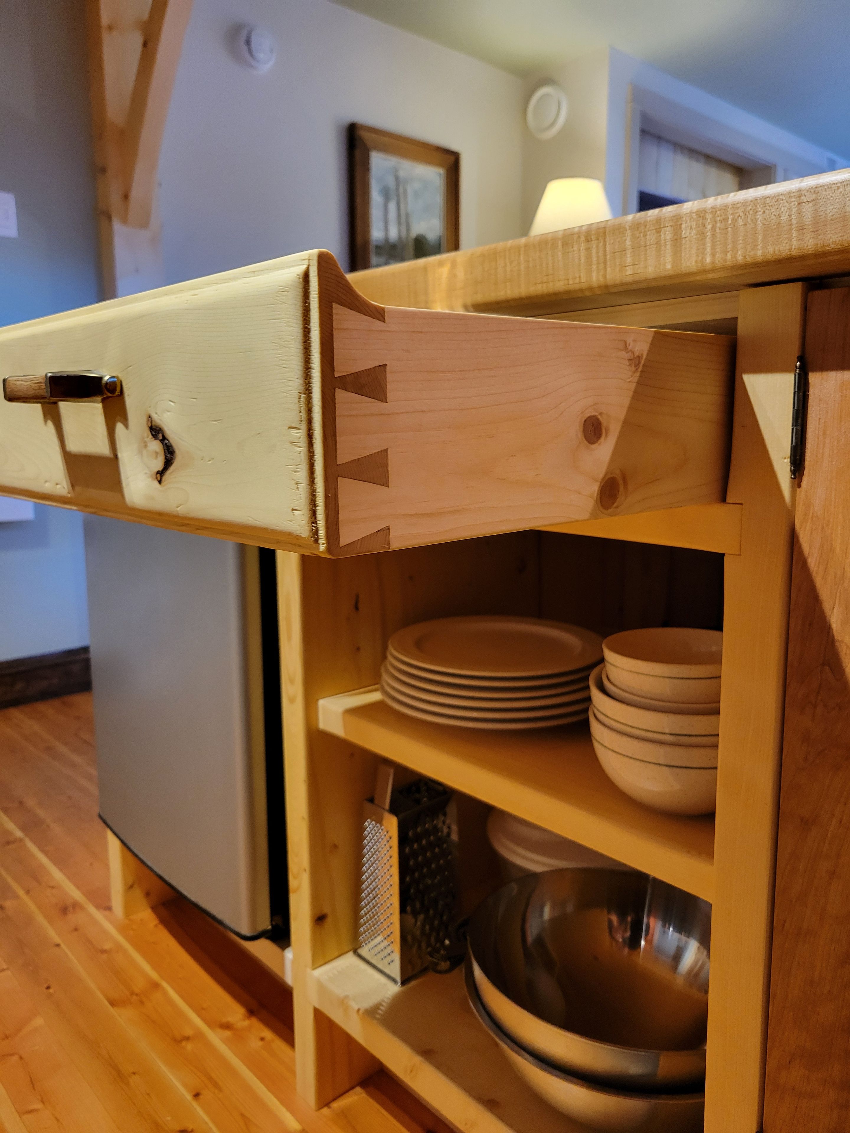 Ein Küchenschrank aus Holz mit einer Schublade, Regalen für Teller und Schüsseln sowie einer Reibe.