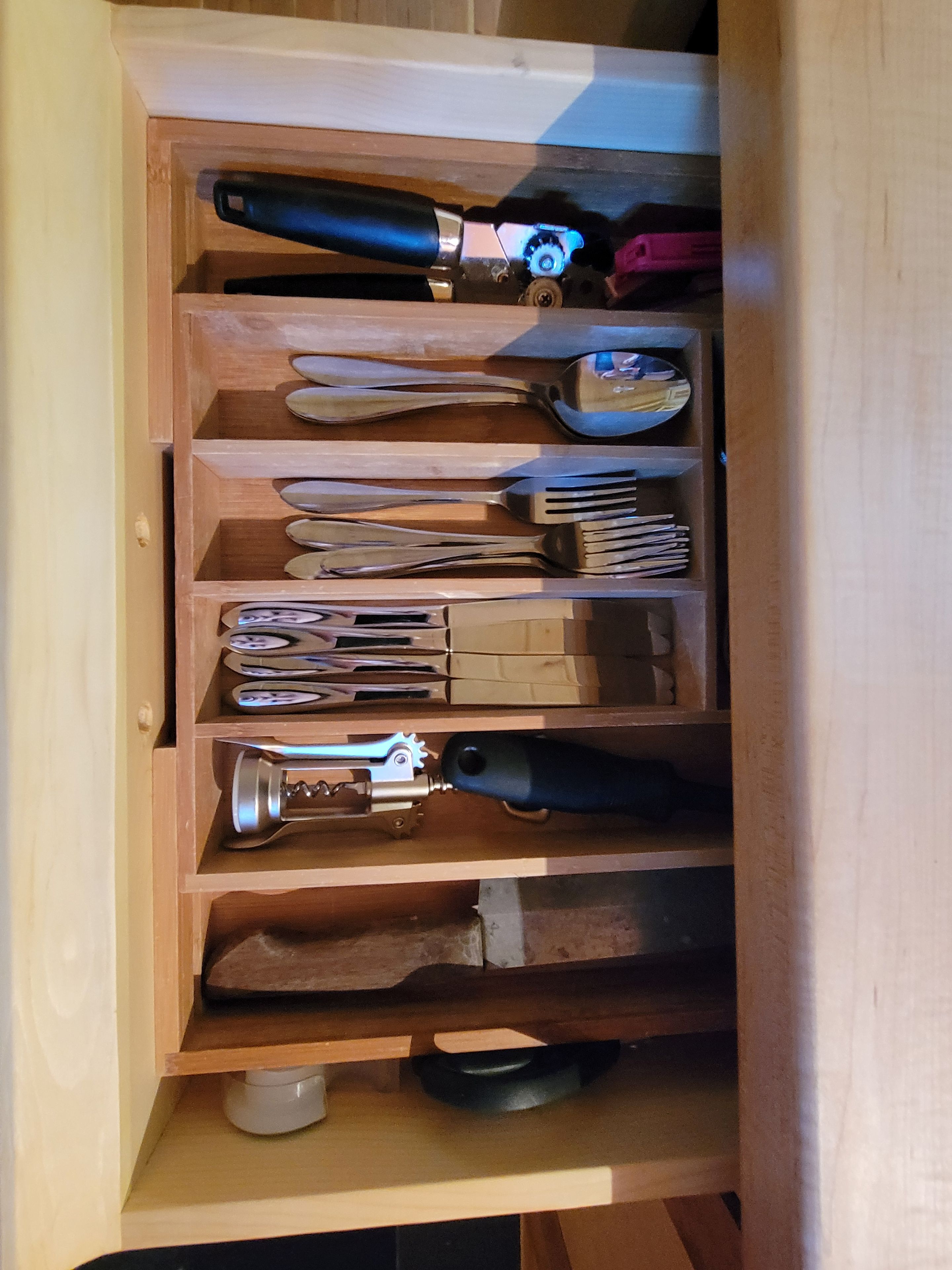 Eine Schublade mit verschiedenen Werkzeugen, darunter ein Messer, eine Schere und ein Flaschenöffner.