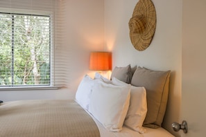 A bedroom with a bed, a lamp, and a wall-mounted decorative item. - Little Eden by Waiheke Pure (Waiheke Island)