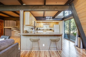 A modern kitchen with wooden cabinets, a marble countertop, and two bar stools. - 1 Woodland Walk to the SR Village with hot tub, fireplace & patio (Sunriver)