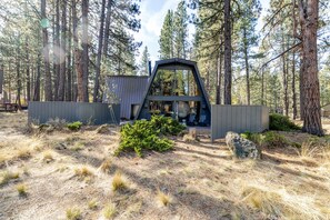 A modern cabin with a triangular roof, surrounded by a forest. - 1 Woodland Walk to the SR Village with hot tub, fireplace & patio (Sunriver)
